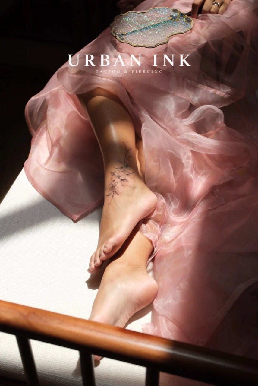 A delicate floral ankle tattoo photographed in warm studio light